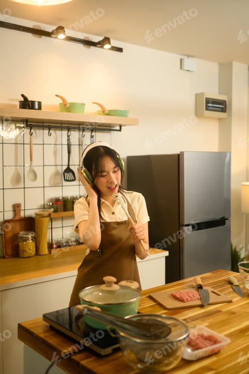 Preview: Happy young woman listening to music while preparing a homemade spaghetti in a kitchen