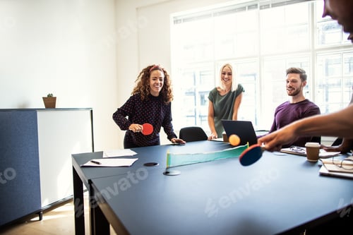 Preview: Laughing colleagues playing table tennis together on a boardroom table