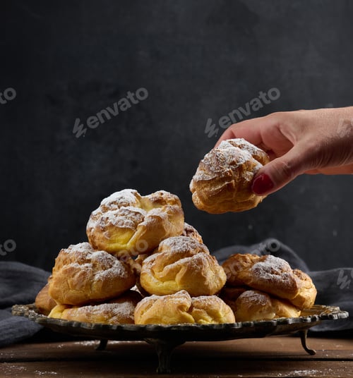 Preview: Baked eclairs with custard cream on a metal round plate sprinkled with powdered sugar