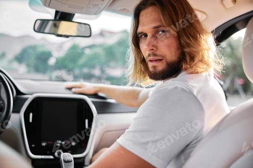 Preview: A young man with long hair and a beard sitting in a car, looking back with a thoughtful expression