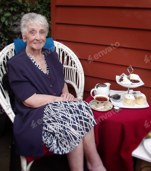 Preview: Senior lady enjoying scones with jam and cream for afternoon tea at a cafe