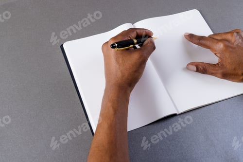 Preview: Hands of biracial man holding pen and writing in notebook with copy space on grey background