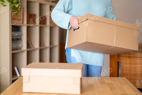 Preview: Woman is carrying a cardboard box while organizing her new house