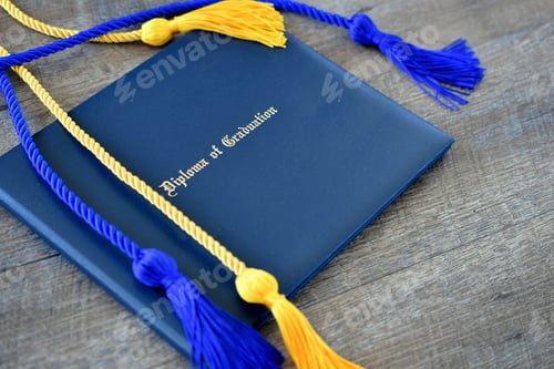 Preview: Flat lay of a Diploma of Graduation with honor cords on a simple wooden background.