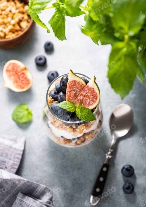 Preview: Delicious natural yogurt with muesli, figs and berries in a glass on a blue background close up.