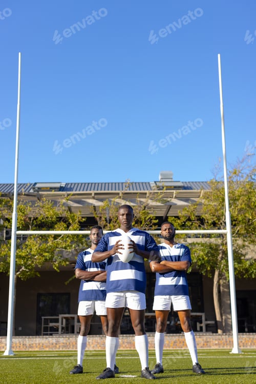 Preview: Three African American young male athletes holding rugby ball on field outdoors, copy space