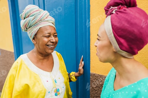 Preview: Happy african mother and her daughter wearing afro clothes while talking in front of their house