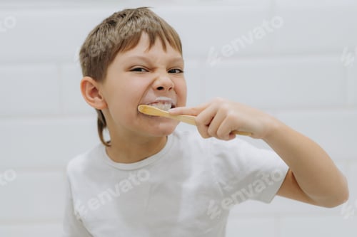 Preview: cute 8 years old boy brushing teeth with bamboo tooth brush in bathroom. Image with selective focus