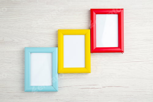 Preview: Close up view of three empty picture frames in different colours on white wooden stripped background