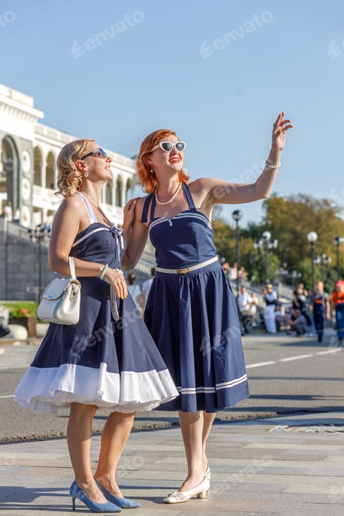 Preview: Two girls dressed in vintage nautical style dresses on the embankment of the river station, port.