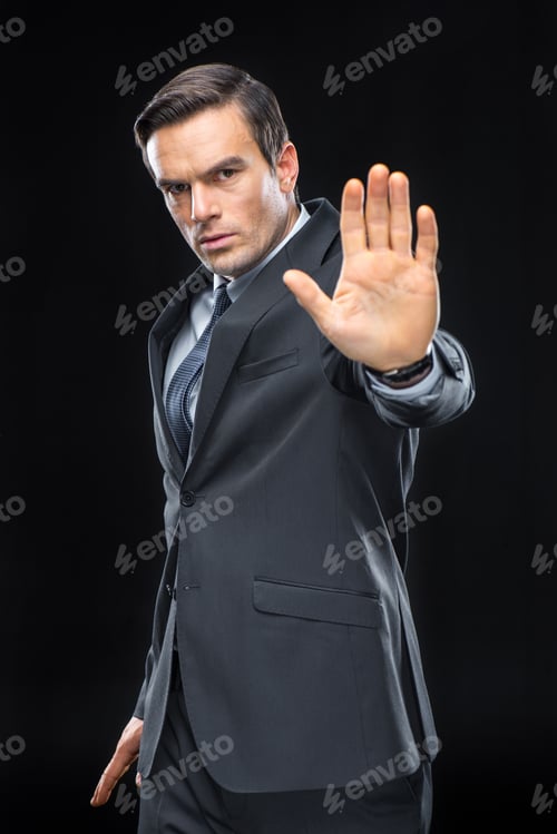 Preview: Handsome businessman gesturing with palm and looking at camera isolated on black