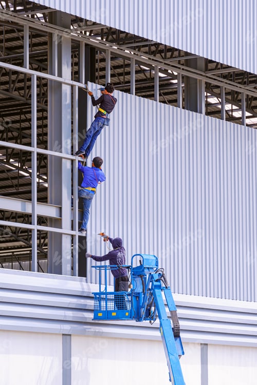 Preview: Construction workers with articulated boom lift installing aluminum sheets on factory building wall