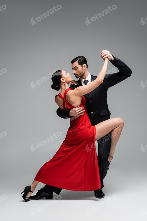 Preview: Full length of elegant couple dancing tango on grey background