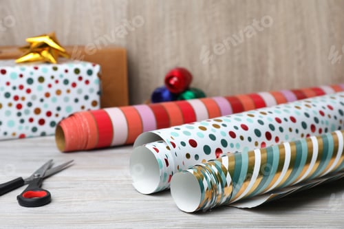 Preview: Different colorful wrapping paper rolls and scissors, on white wooden table, closeup