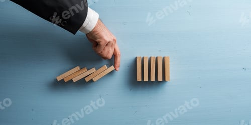 Preview: Hand of a businessman interrupting collapsing dominos with his finger