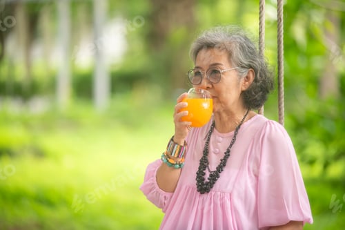 Preview: elderly women are sitting on wood swing and drink orange juice outdoors in the greenery around time