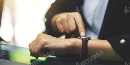 Preview: A business woman pointing at a wristwatch on her working time while waiting for someone in office