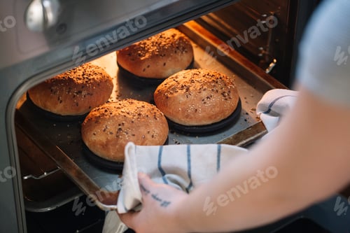Preview: Woman taking homemade vegan burger rolls out of oven