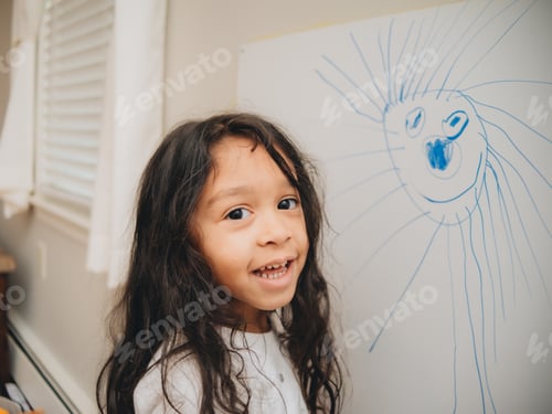 Preview: Diverse pre school girl at home drawing funny characters and faces on dry erase board
