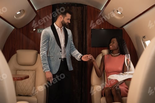 Preview: handsome, elegant man holding hand of smiling african american woman sitting at table near glass of