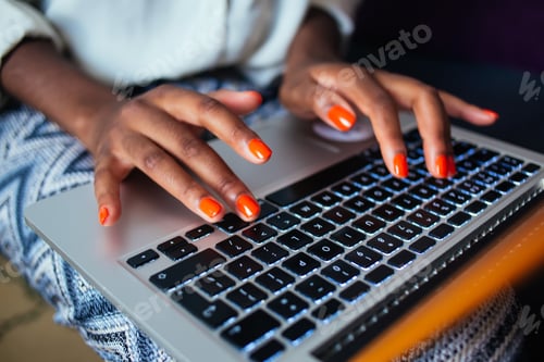 Preview: Cropped image of female's fingers with perfect orange nail polish over keyboard of netbook