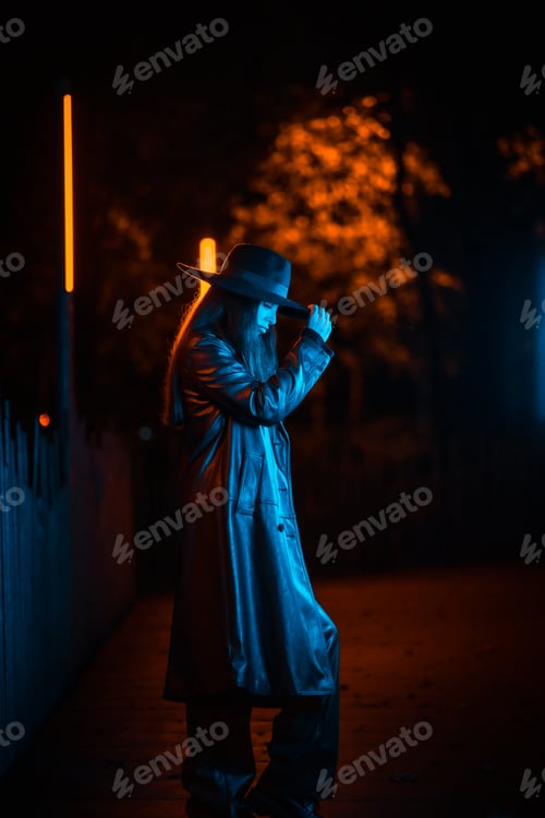 Preview: Caucasian brunette girl with hat at night in a park illuminated with blue light