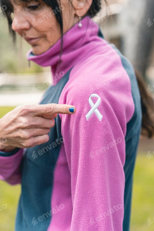 Preview: Woman pointing to an embroidered cancer awareness ribbon with her finger. Vertical shot
