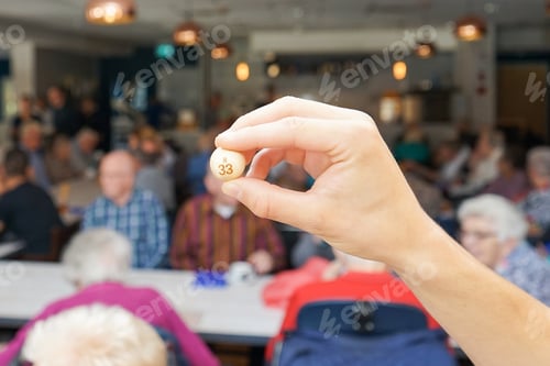 Hand Holds Bingo Ball With Group Playing
