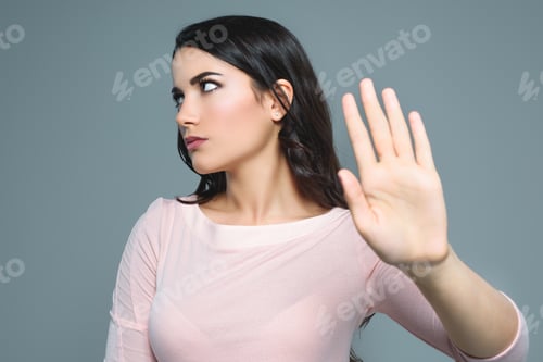 Preview: beautiful girl with bad mood gesturing stop symbol, isolated on grey