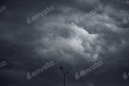 Preview: Silhouette of street lamp post against dark stormy clouds in summer