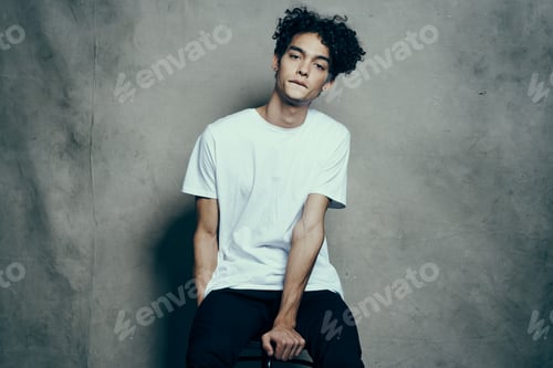 Preview: cute guy with curly hair sitting on a chair studio