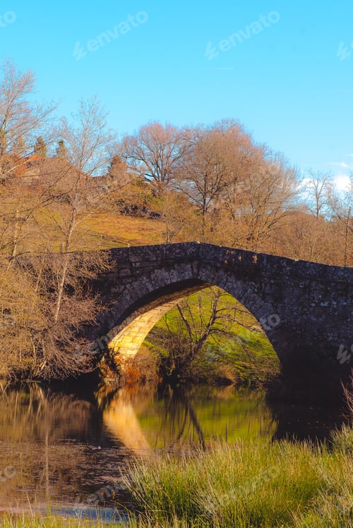 Preview: Old bridge over calm river in autumn countryside