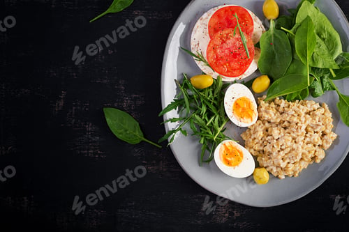 Preview: Breakfast oatmeal porridge with boiled egg, tomatoes sandwich, arugula and spinach.