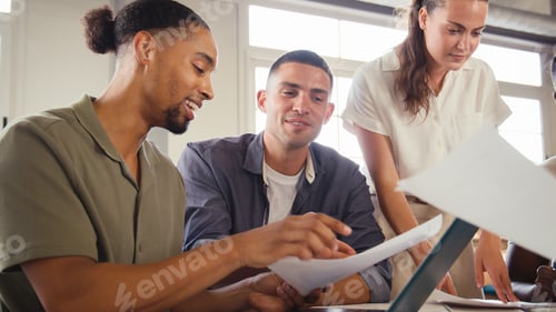 Preview: Multi-Cultural Business Team Meeting Around Desk In Modern Open Plan Office Discussing Documents