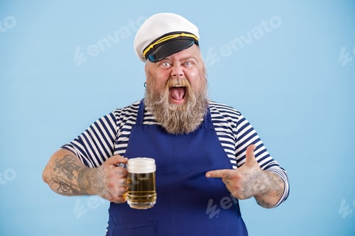 Preview: Excited bearded man with overweight in sailor suit points onto beer on light blue background