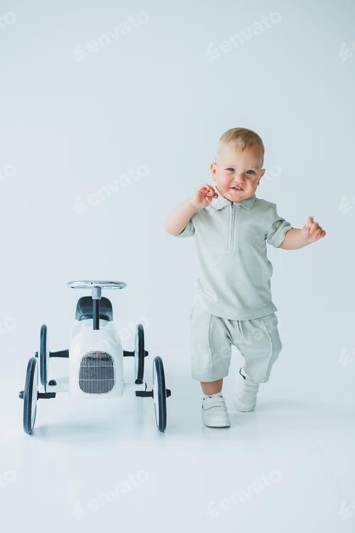 Preview: Stylish one-year-old boy in a suit with shorts and a T-shirt rides a car. Toddler boy on a white