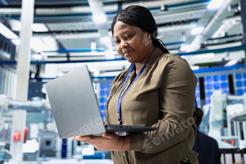 Preview: Female tech specialist reviewing assembly line insight on laptop