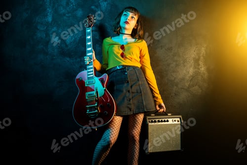 Preview: Woman Holding Guitar and Amplifier in Dramatic Lighting
