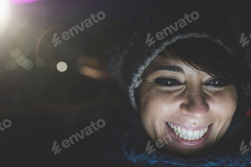 Preview: Illuminated close up of happy woman wearing knit hat at night