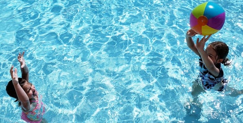 Preview: Day at the pool with beach ball for generation z sisters in the blue water.