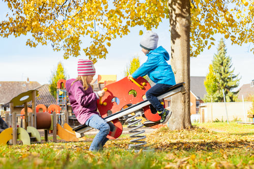 Preview: Children, a boy and a girl, swing on a swing in the fall on a playground.