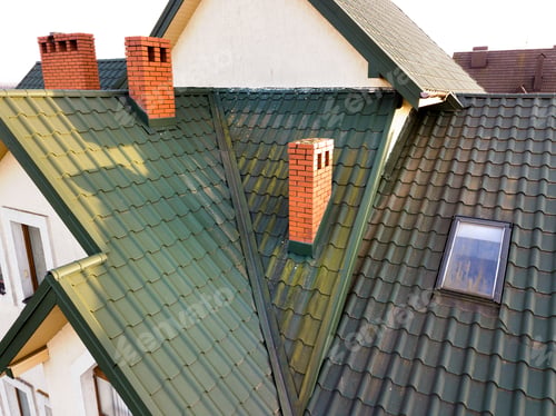 Preview: Green metal shingled house roof with attic plastic window and brick chimney.