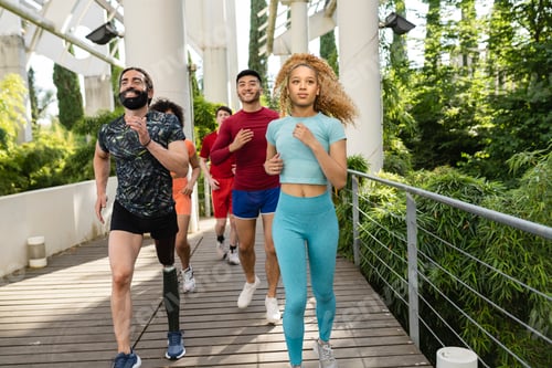 Preview: Multiracial group of runners running in an park with plants.