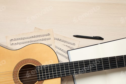 Preview: Composition with guitar and music notations on light wooden table, flat lay. Space for text