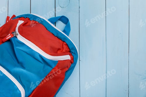 Preview: Colorful backpack rests on light blue wooden surface ready for school or outdoor adventures