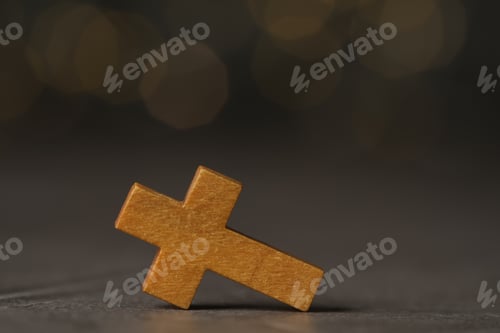 Preview: Wooden Christian cross on grey table against blurred lights, space for text