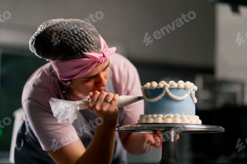 Preview: of a female baker in a professional kitchen decorating a blue cake with cream