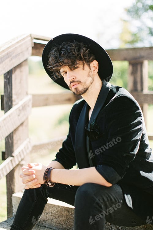 Preview: Man in a black hat sits on the steps near the wooden railing