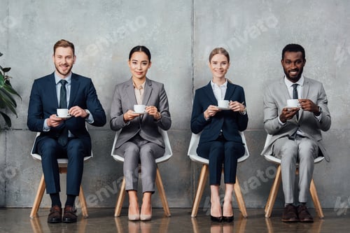 Preview: multiethnic businesspeople sitting on chairs, drinking coffee and looking at camera in waiting hall