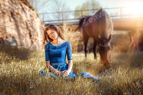 Preview: Beautiful girl in a blue dress is sitting on the grass